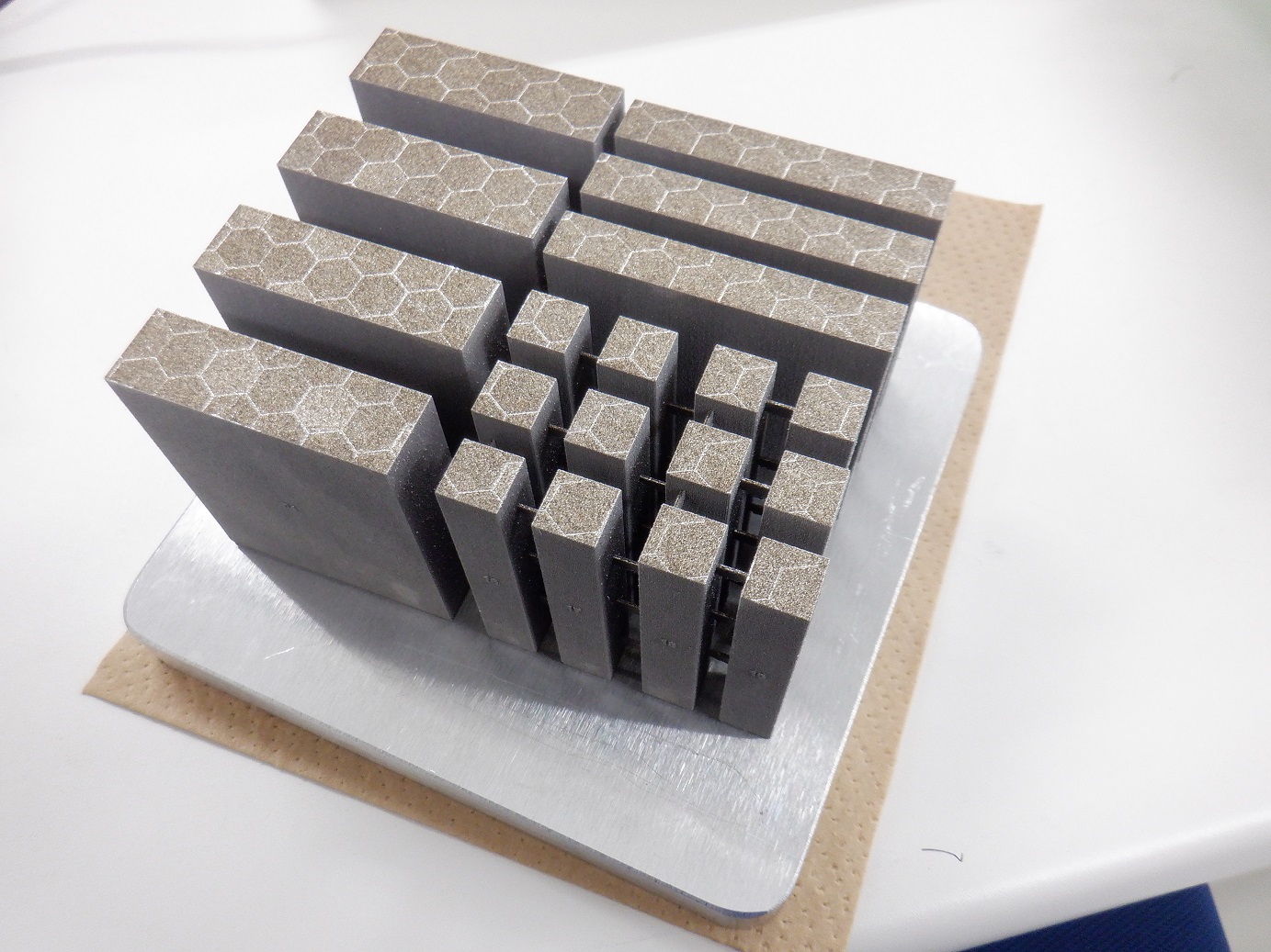 新たに設計した材料を金属3Dプリンタで造った積層造形体（表面の六角形のマークは、レーザー照射のパターンを示す）