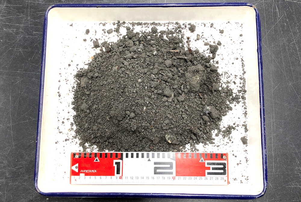 研究で使用する”焼却灰”です。家庭ごみを燃やした後の灰で、これが最終処分場で埋め立て処分されています。意外と砂やレキのように見えるでしょ？よく見ると、ガラス片や陶器、釘なども混じっています。