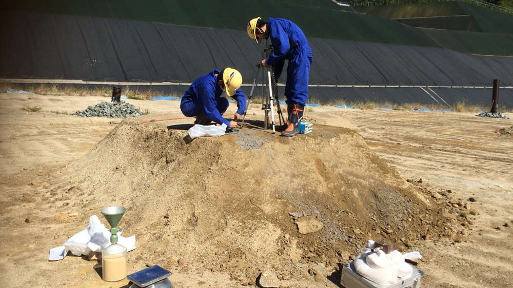 研究室の学生と一緒に、実際の最終処分場で実験をしている写真です。焼却灰で作製したマウンドの強度や密度を測定しています。一部はサンプリングして研究室に持ち帰り、より詳しい実験（強度試験や環境安全性試験など）を行います。