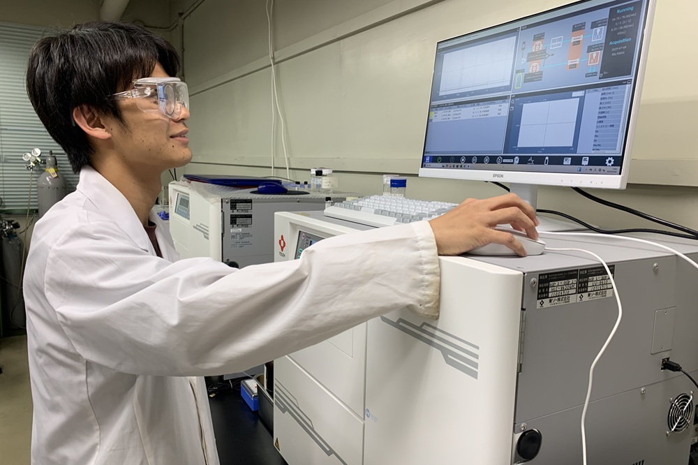 修士課程に在籍する小池さんが、自身で合成した高分子の分子量（分子の長さ）を、ゲル浸透クロマトグラフィー（GPC）という分析手法を用いて測定している様子です。私が所属する学科では、学部3年生の後期から研究活動が始まり、多くの学生がそのまま修士課程へ進学して研究を継続します（他大学や他学科では、学部4年生の前期から研究活動が始まることが一般的です）。研究活動では、学生一人ひとりが自らの研究テーマに取り組みます。課題の設定、仮説の構築、実験の実施、そして得られた結果の考察までを、先輩や指導教員と議論しながら主体的に進め、研究成果を国内外の学会で発表したり、論文を執筆したりします。