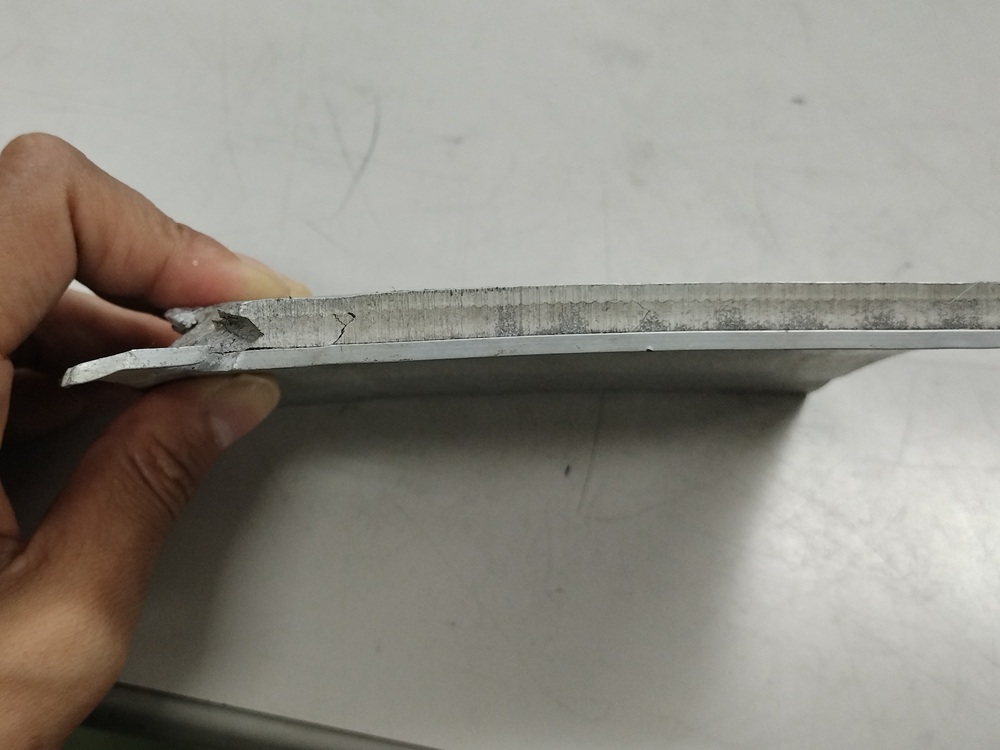 爆着材の写真。中央部がマグネシウム合金で、アルミニウム合金でサンドイッチした接合材。クラック（割れ）が見られる部分もあり、良好な接合が可能な条件の模索が必要です。