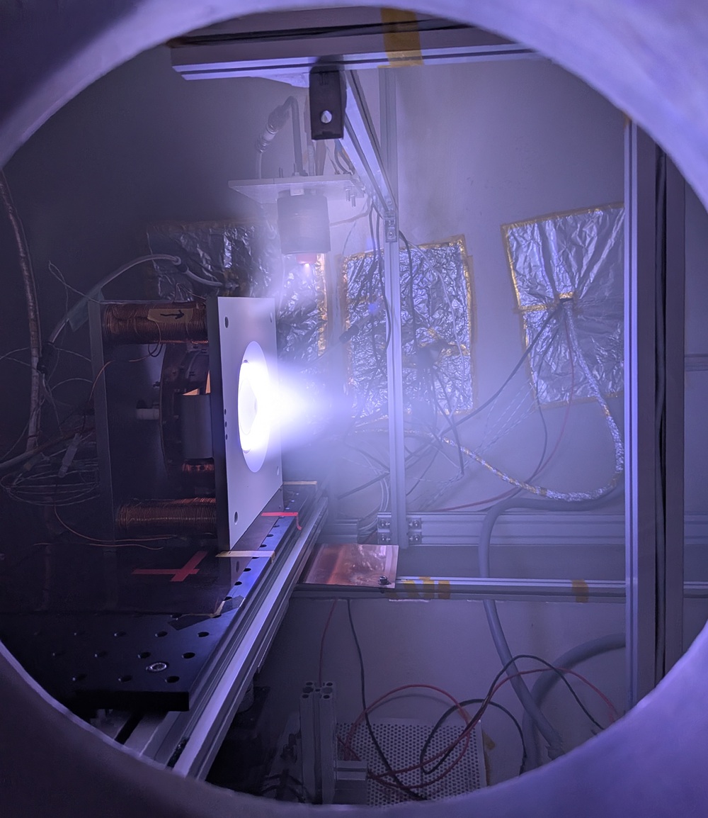 宇宙電気推進機（ホールスラスタ）の実験を行っている様子。宇宙空間を模擬する真空チャンバーの中でプラズマを作ります。