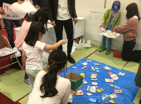 ゼミ生が自分たちで考えて作った、子どもが楽しめる防災釣りゲームの様子です。魚には備蓄に必要なものや避難時の注意点が書かれており、参加者はそれを釣りながら学びます。1回目は説明なしで実施し、終了後に点数（重要なものほど高い点数）をもとに、参加者になぜこのような点数になったのかを考えてもらうとともに解説を行います。その後、2回目を実施することで、実際に備蓄の行動を学んでもらいます。1回目と2回目の点数を比較することで、どれほど学んだのかも評価しました。