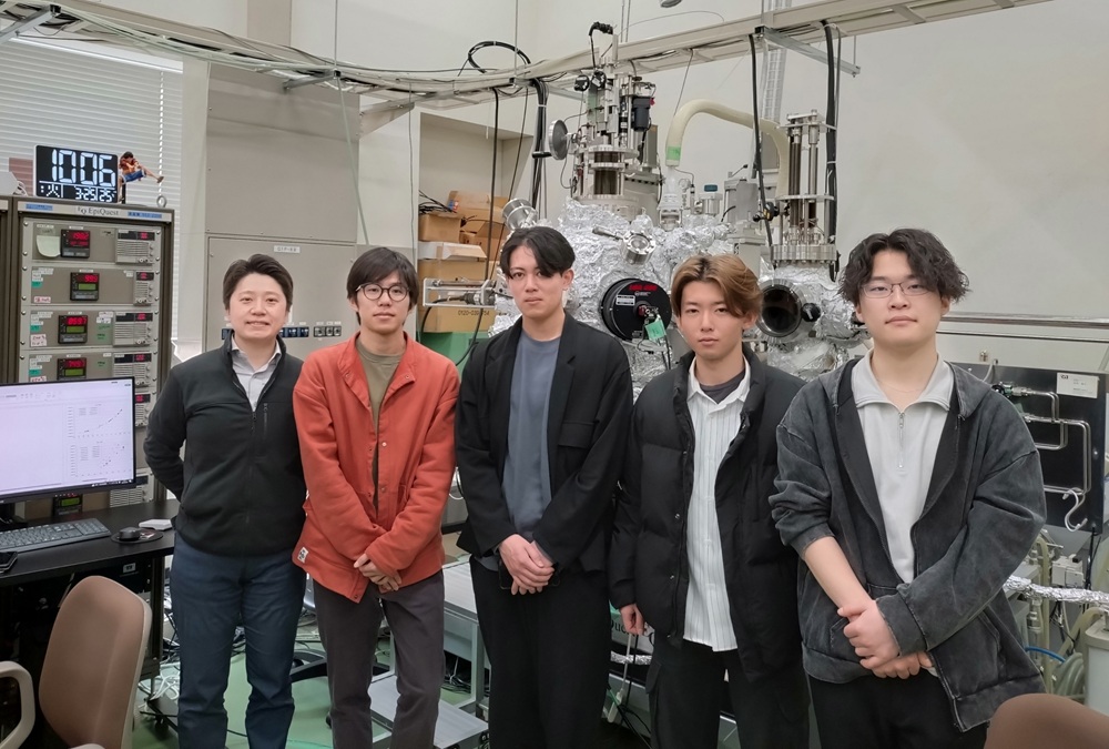 超高真空（非常に低い圧力）下で窒化物半導体を結晶成長する装置の前で、学生と。身長よりも大きな装置を使って実験します。