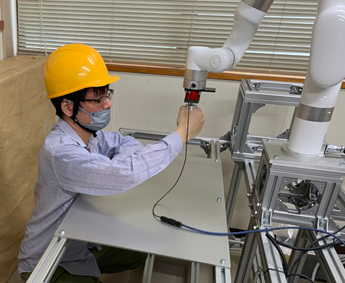 人にロボットの手先につけたハンドルを握らせロボットの手先を動かすことで、ヒトの腕部のリハビリ動作に関する実験を行っている様子です。