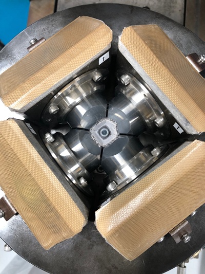 In the cubic-anvil type high-temperature high-pressure apparatus, the sample and heater are embedded inside the crushed, dice-shaped object in the center, after the heat treatment of the sample. The circle at the top is an electrode for electrical contact with the upper anvil.