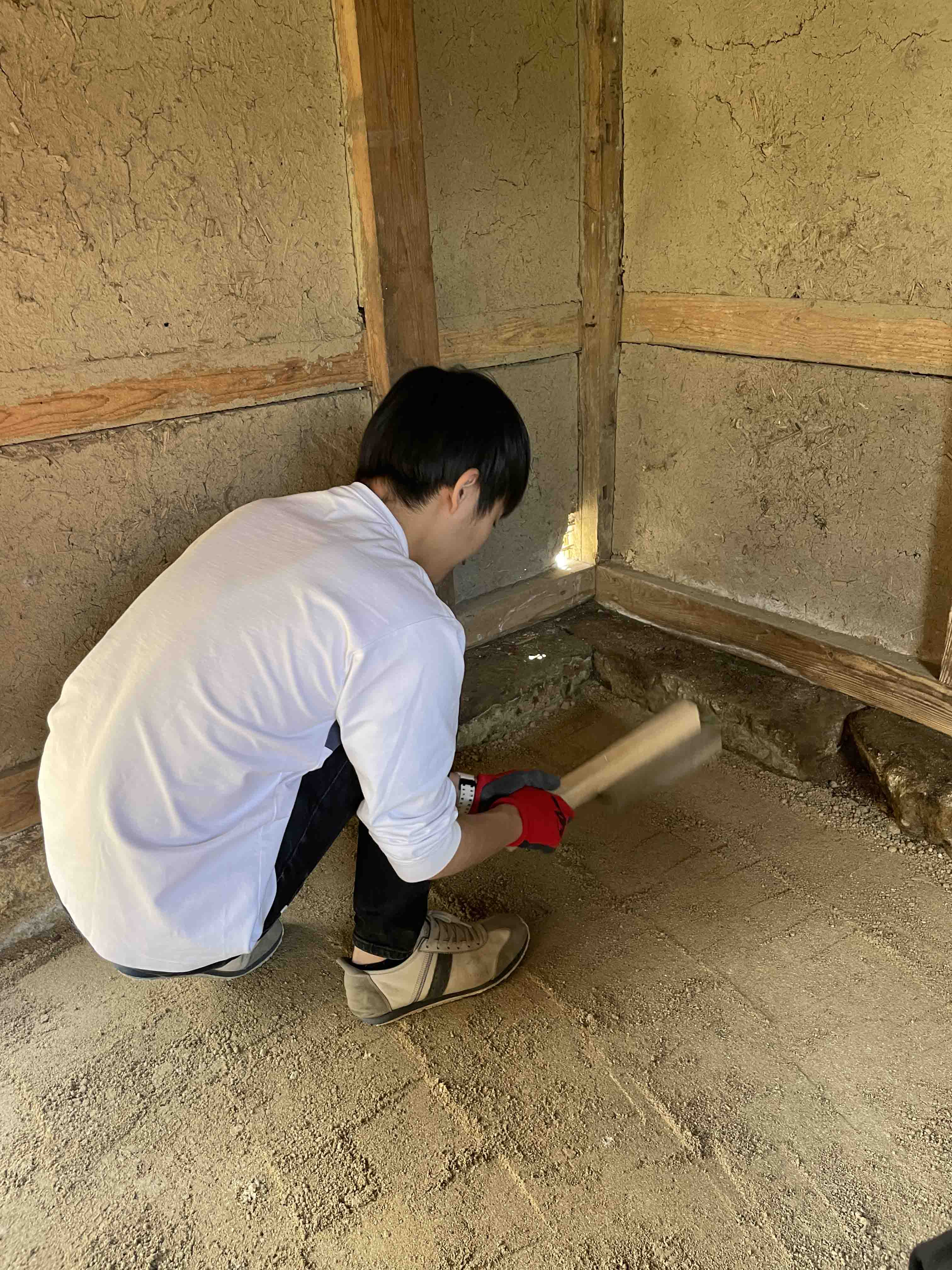 土間の修復をしています。伝統的な住宅では土間を作るために三和土（たたき）という方法が用いられます。砂に石灰とにがりを混ぜて、文字通り「叩く（たたく）」ことで締め固められ、土間ができあがります。