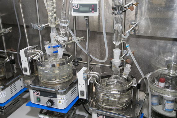 新規抽出剤(有機化合物)を合成するための実験装置。この実験では、フラスコや冷却管、滴下漏斗などの様々なガラス器具を使用します。